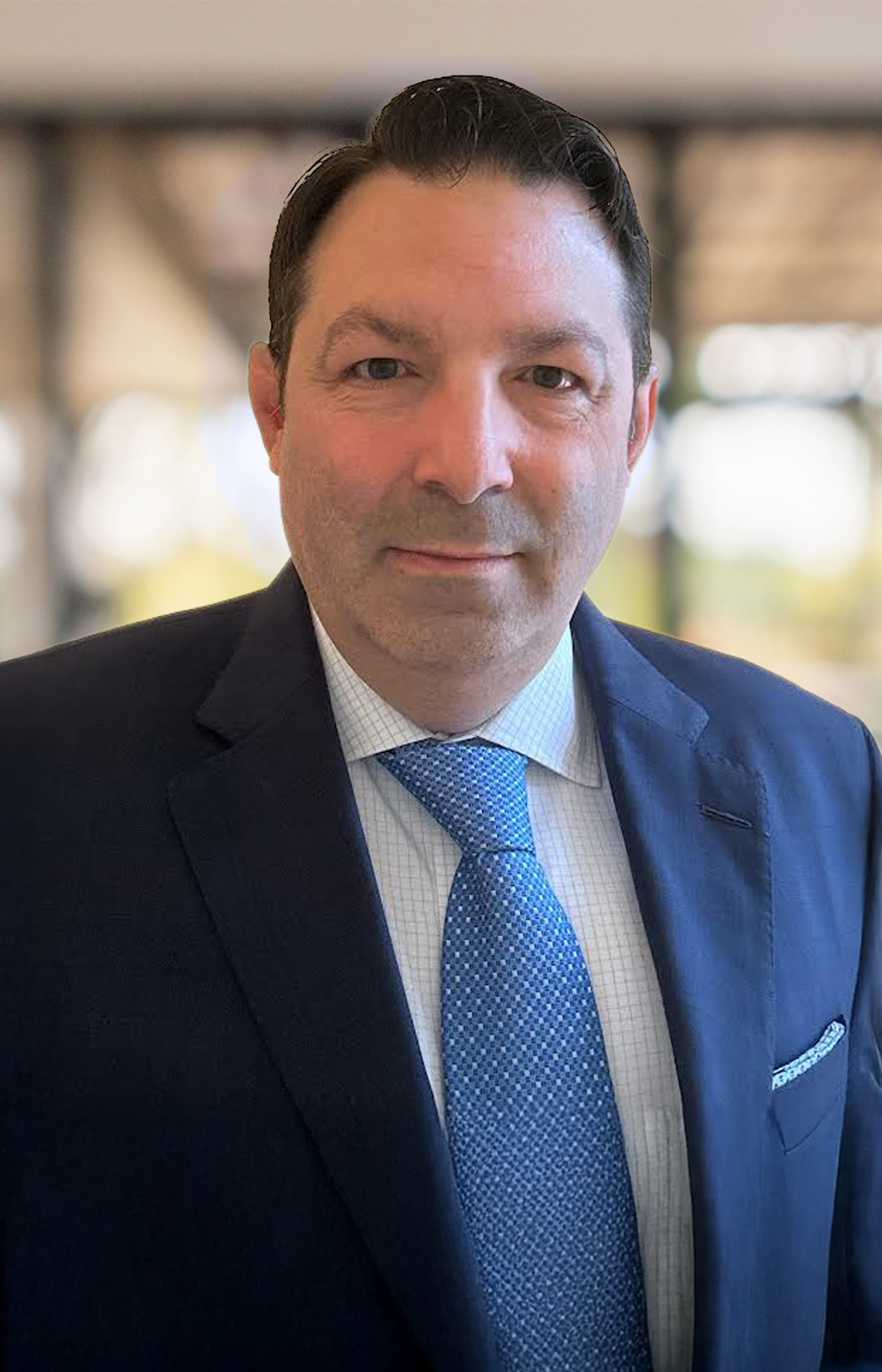 A man, identified as Michael J. Fleres, in a dark suit, light blue dress shirt, and patterned blue tie stands indoors with a blurred background. He has short dark hair, light skin, and a neutral expression.